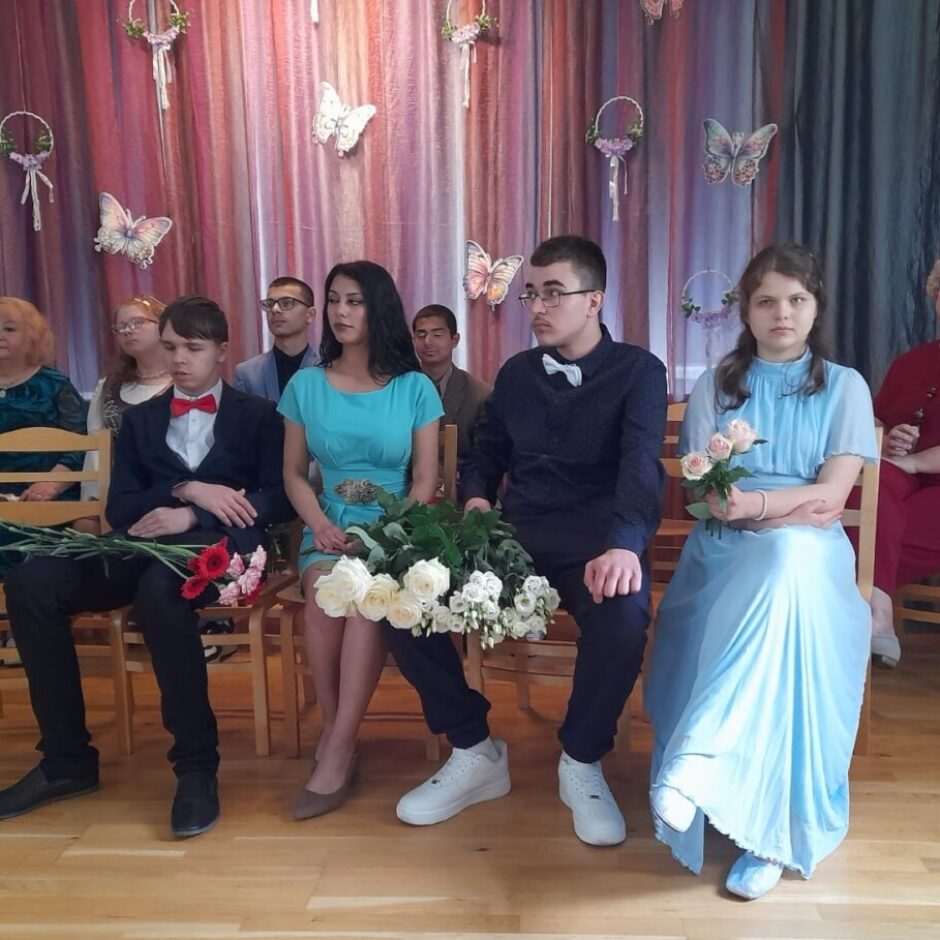 skolēni sēž zāles priekšā izlaidumā