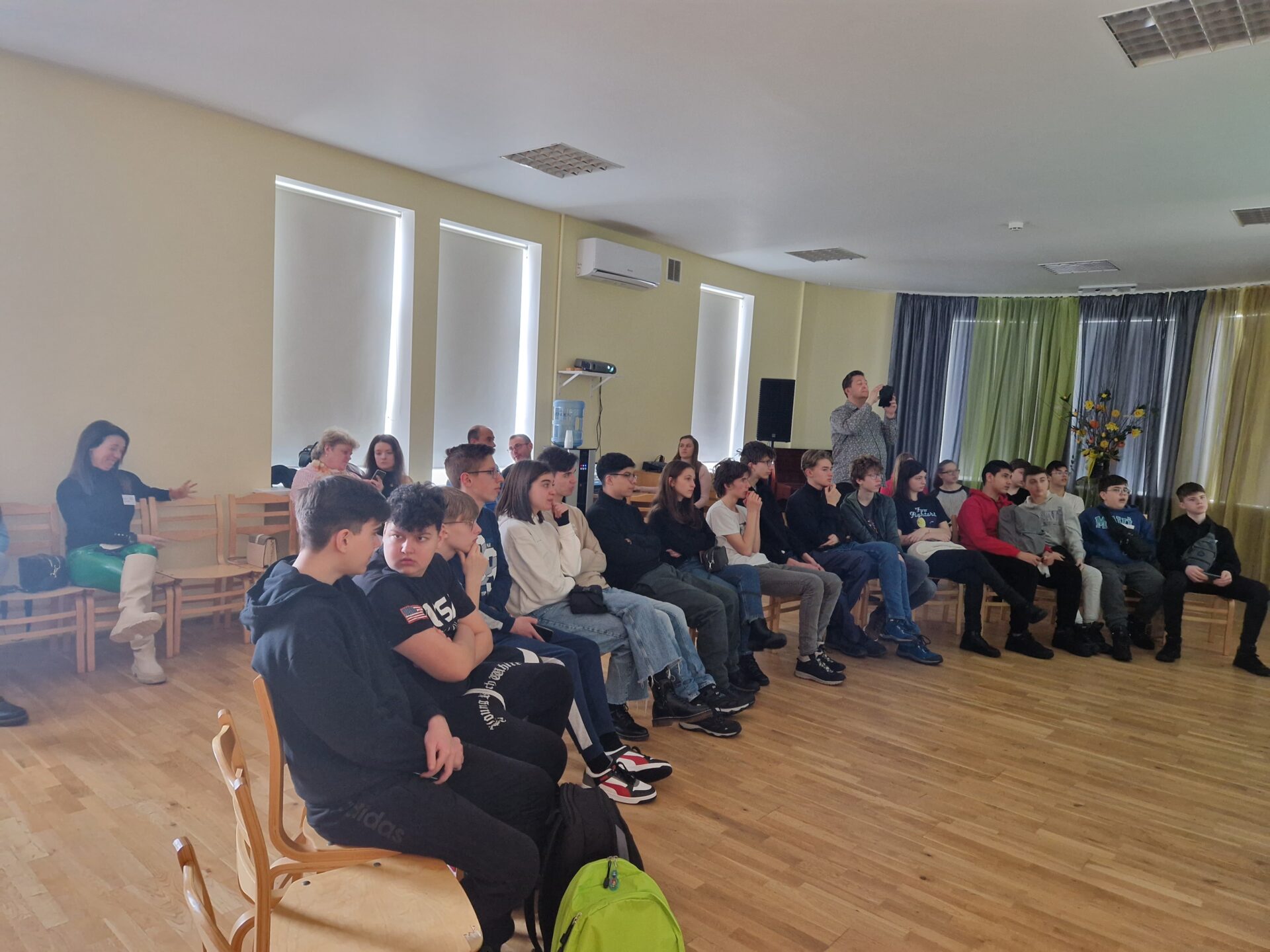 Pasākuma dalībnieki klausās prezentāciju skolas zālē