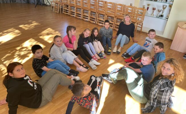 Skolēni sēž aplī uz grīdas ar dažādām kurpēm