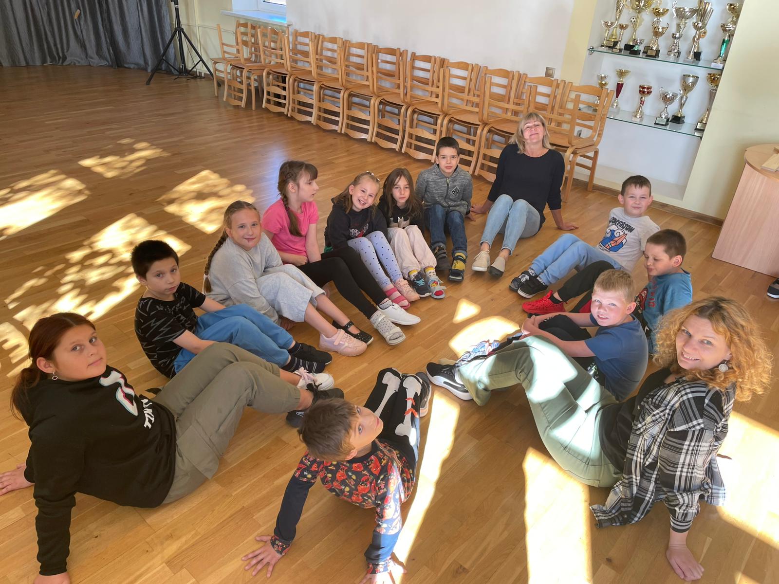Skolēni sēž aplī uz grīdas ar dažādām kurpēm