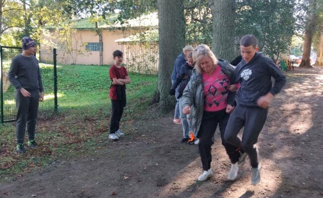 Skolotāja un skolēni skrien ar kopā sasietām kājām